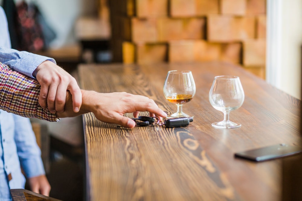 Main retenant la main d'une personne souhaitant prendre ses clés de voiture avec verre d'alcool vide sur la table. alcool au volant et sanction
